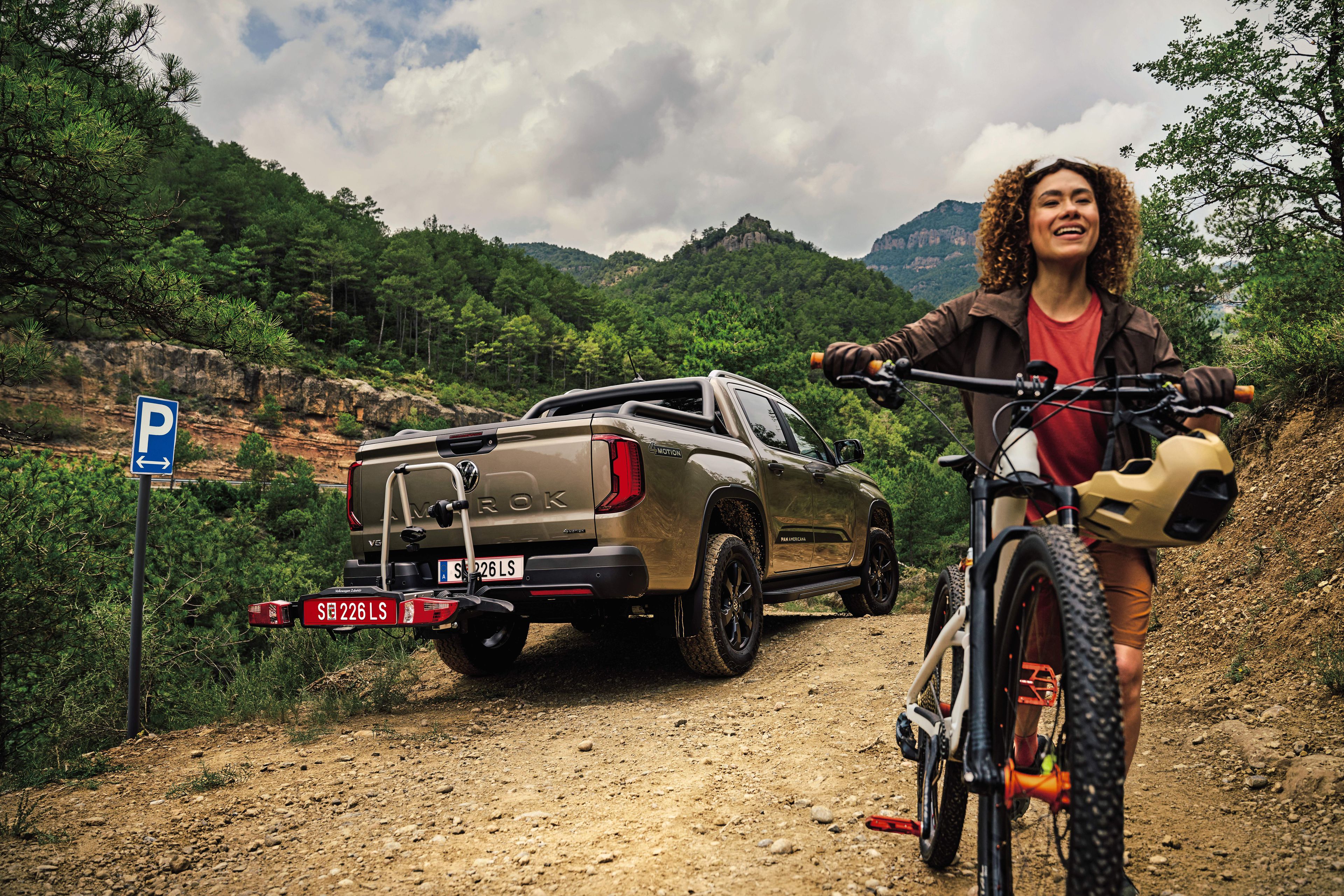 Amarok parkt im Wald, Frau mit Mountainbike fährt davon weg